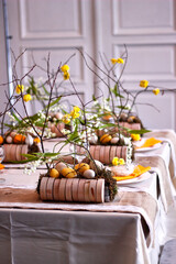 Easter table setting in yellow colors with floral arrangements of yellow flowers, eggs and lilies of the valley