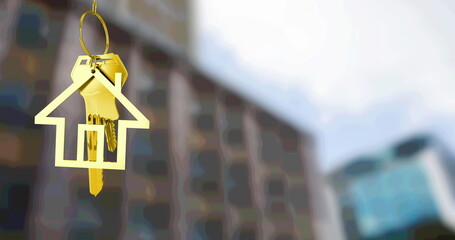 Image of gold house key fob and key, hanging in front of blurred city building