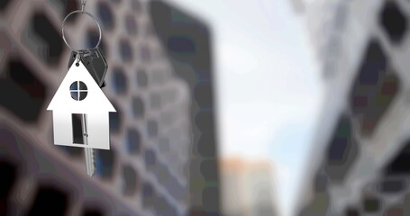 Image of silver house key fob and key, hanging in front of blurred city high rise buildings