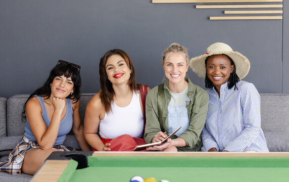 Diverse group of diverse female friends sitting on couch, smiling and enjoying leisure time, at home