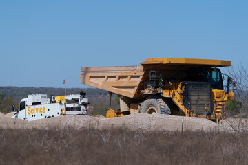 Very large dump truck is getting a tire change from a mobile service truck on-site at a rock quarry in West Texas.