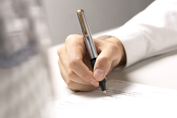 Close-up shot of a hand signing a document with a pen. Ideal for illustrating legal agreements,...