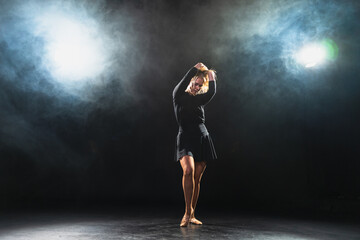 Contemporary woman dancer posing on black background with smoke. Adult female artist performer dancing with expression. Modern ballerina dancing in darkness. Passion dance in dark. Flexibility balance