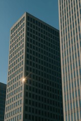 Obraz premium Sunlight reflecting on geometric facades of tall urban buildings against clear blue sky