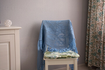 A blue shawl knitted using the fillet knitting technique hangs on a white chair