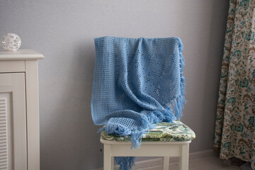 A blue shawl knitted using the fillet knitting technique hangs on a white chair