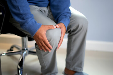 An office staff is suffering the Osteoarthritis and causes knee pain, swelling, redness, stiffness in the knee, clinging noise in the knee, he is massaging and rubbing the pain area to get relief.