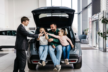 A happy young family gets the keys to their new car at a modern car dealership. The end of a test...