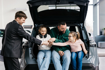 A happy young family gets the keys to their new car at a modern car dealership. The end of a test drive or purchase of a new car.