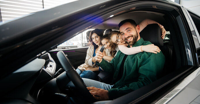 A happy young family in a modern car dealership after completing the purchase of a new family car. The concept of renting, test-driving a car. 