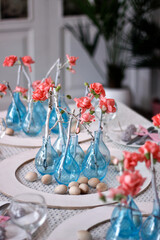 modern Easter table setting with blue vases, pink flowers and wooden eggs in a white interior
