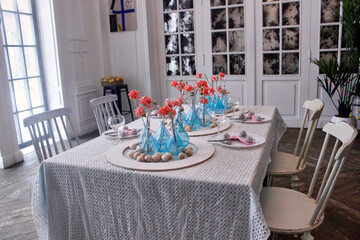 modern Easter table setting with blue vases, pink flowers and wooden eggs in a white interior