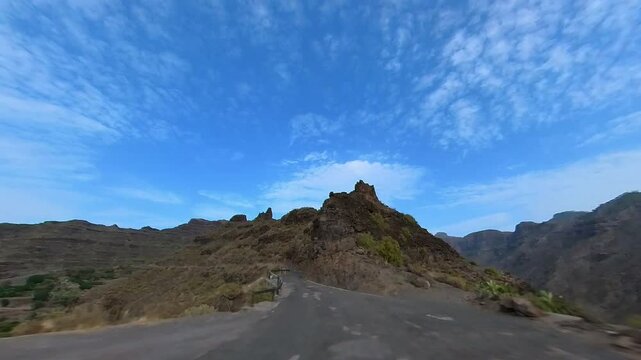 Wide-angle video showing the GC-606 road winding through arid, mountainous terrain in Gran Canaria, leading to Carrizal de Tejeda. Captured on a sunny day