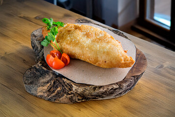 Homemade Italian panzerotto on a wooden cutting board, with cherry tomatoes and parsley, on a rustic table. Homely and cosy style, ideal for traditional Italian cooking themes