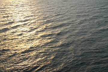 The golden reflection of the sunset rays seems to color the surface of the wavy sea as evening approaches.