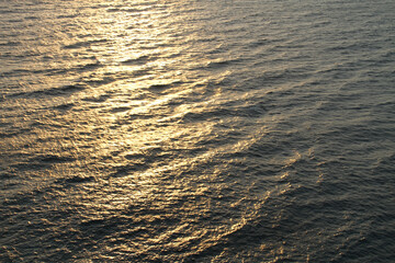 The golden reflection of the sunset rays seems to color the surface of the wavy sea as evening approaches.