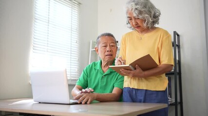 Elderly couple showing teamwork and focus while discussing finances at home with laptop and notebook. - Powered by Adobe