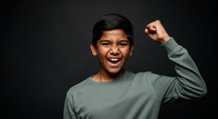 Fototapeta premium Energetic hispanic young male celebrating success with raised fist on dark background