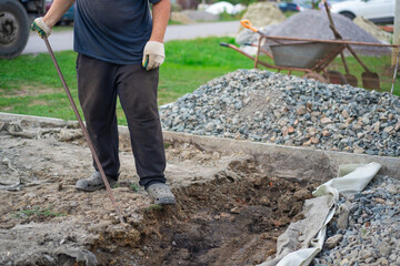 A man in old clothes is chiseling the ground with a crowbar