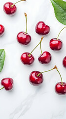 Ripe red cherries scattered on marble with green leaves