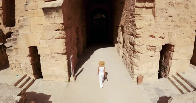 Stylish woman with hat exploring ancient colosseum amphitheater in El Jem, Tunisia, under bright sunlight