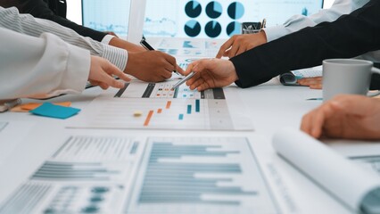 Participants engage in a collaborative business meeting, analyzing detailed charts and graphs on the table, showcasing teamwork in a modern office setup. SACTR