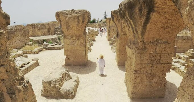 Ancient Roman ruins with woman tourist exploring an archaeological Historic Roman Baths of Antoninus  site in Tunisia, aerial shot