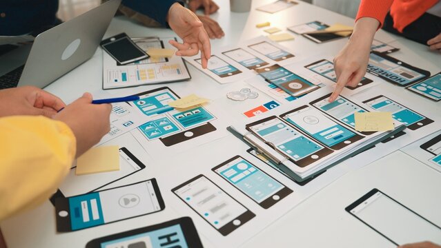 A team of designers collaborates on user interface designs using smartphones and tablets in a creative workspace filled with notes and sketches. SACTR