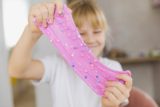 Adorable little girl holding a slime toy, a popular homemade toy all over the world. A child plays with slime and stretches it.