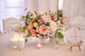 Elegant table setting for wedding banquet close-up. Festive bouquet with fresh tender pink flowers, candles and cards on dining table at restaurant