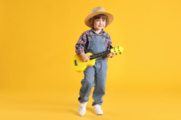 Cute little boy playing toy guitar on yellow background