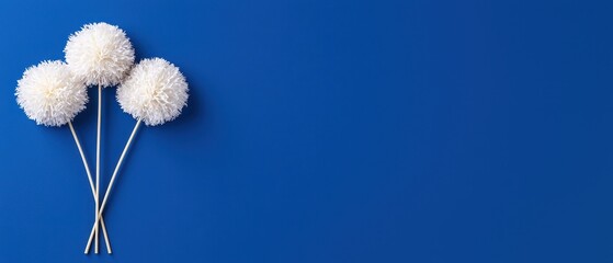 Three fluffy pom-poms on sticks against a vibrant blue background.