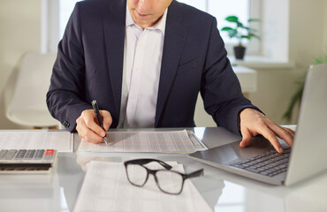Young business man accountant in suit working at desk with financial documents on his workplace in...