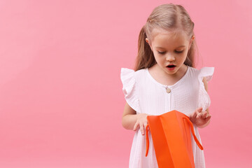 Little girl with shopping bag on pink background, space for text
