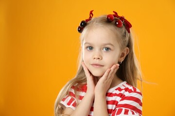 Cute little girl wearing beautiful bows with cherries on orange background. Space for text