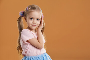 Cute little girl wearing beautiful hair accessories on light brown background. Space for text