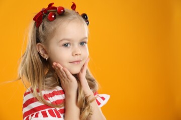 Cute little girl wearing beautiful bows with cherries on orange background. Space for text
