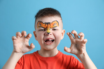 Cute boy with tiger face painting on light blue background