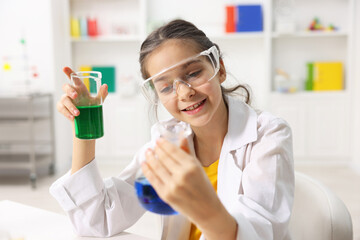 Little girl doing chemical experiment at desk indoors