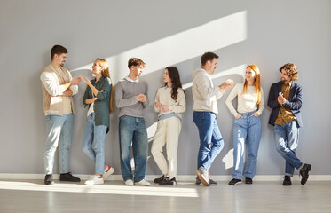 Group of young people casually chatting while leaning against gray wall in modern space. Close...