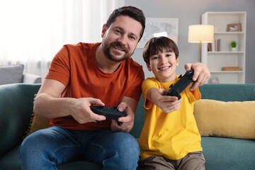 Happy father and his son playing video games on sofa in living room