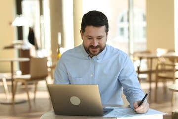 Handsome business owner working with laptop at table in his cafe