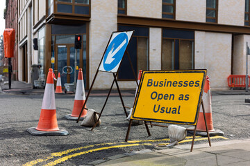 Businesses Open as Usual Sign at Roadworks Road Junction with Traffic Cones and Pass on Left Arrow