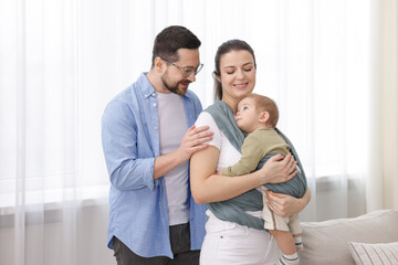 Portrait of happy family indoors. Mother holding her child in sling (baby carrier) at home