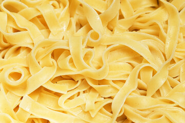 Boiled yellow pasta texture. Closeup of tagliatelle background. Classic Italian ingredient. Simple food backdrop. Macro view of cooked noodles.