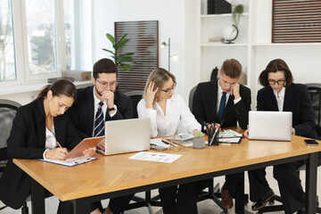 Coworkers with different devices working together at wooden table in office