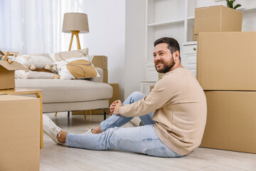 Moving day. Man resting on floor near cardboard boxes in his new home