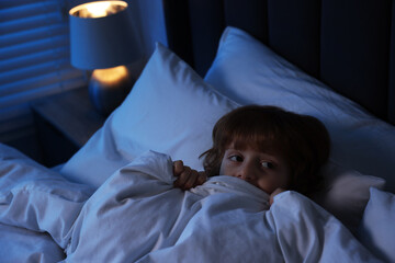 Scared boy hiding under duvet in bed at night