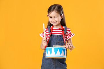 Cute girl playing toy drum on yellow background