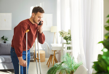 Injured man posing on crutches after physical injury, has problem with mobility, making call via...
